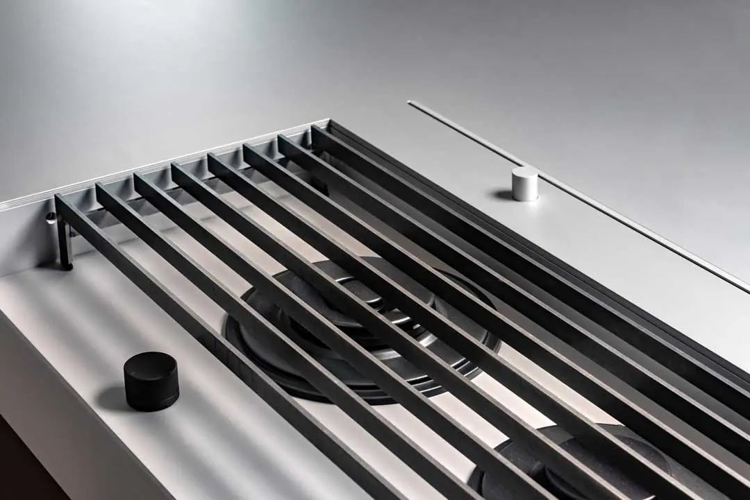 Nahaufnahme eines modernen, minimalistischen Gasherds aus Aluminium mit schwarzen Rosten, zwei Brennern und zwei runden Bedienknöpfen auf einer glatten, hellen Oberfläche. Das Design des Designers Jan-Erik Heym zeichnet sich durch klare Linien und eine moderne Ästhetik aus.