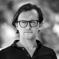 Murat Özçelic blickt in die Kamera. Er trägt ein dunkles Button-up-Hemd. Der unscharfe Hintergrund im Freien,